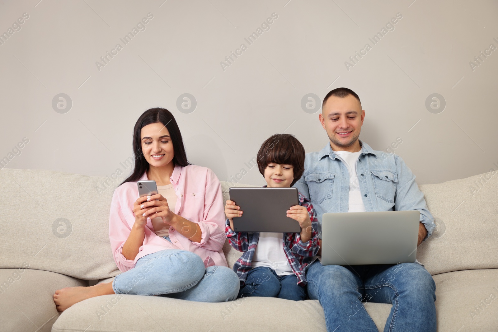 Photo of Happy family with gadgets on sofa at home