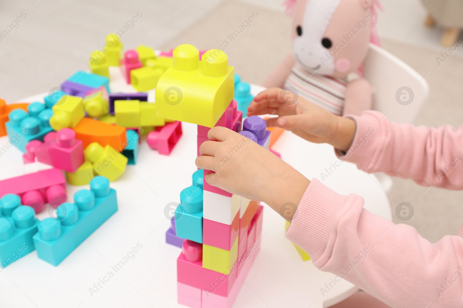 Photo of Little girl playing with colorful building blocks at table indoors, closeup