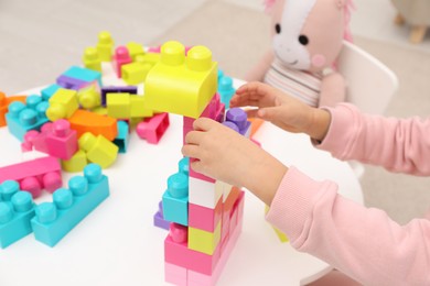 Photo of Little girl playing with colorful building blocks at table indoors, closeup