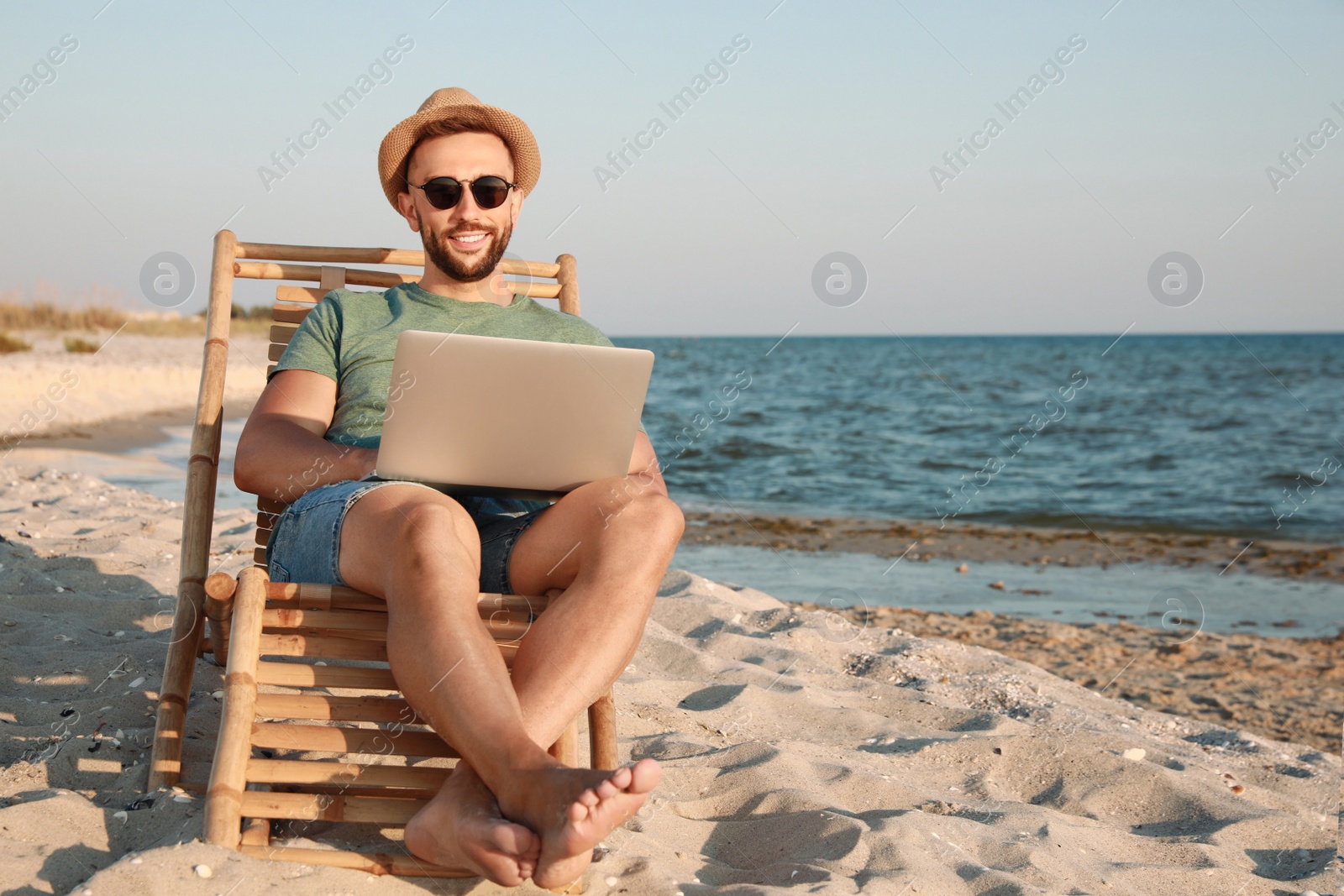 Photo of Man working with laptop in deck chair on beach. Space for text