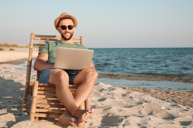 Man working with laptop in deck chair on beach. Space for text