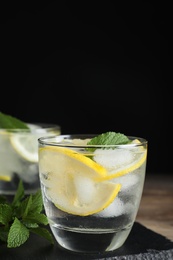 Glass of cocktail with vodka, ice and lemon on wooden table against black background. Space for text