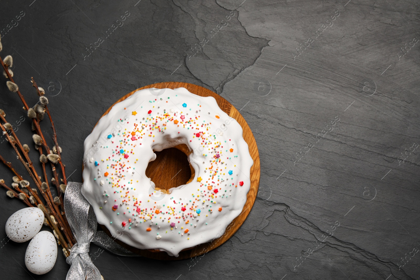 Photo of Delicious Easter cake decorated with sprinkles near eggs and willow branches on black textured table, flat lay. Space for text