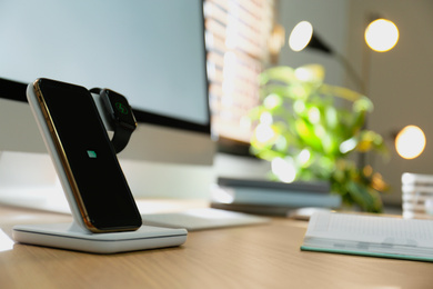 Photo of Modern workplace with smartphone and watch charging on wireless pad