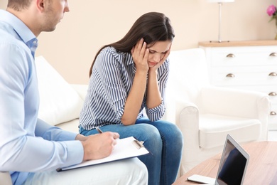 Depressed young woman having appointment with psychologist in office