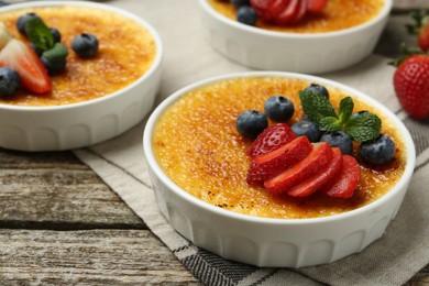 Delicious creme brulee with berries and mint in bowls on wooden table, closeup