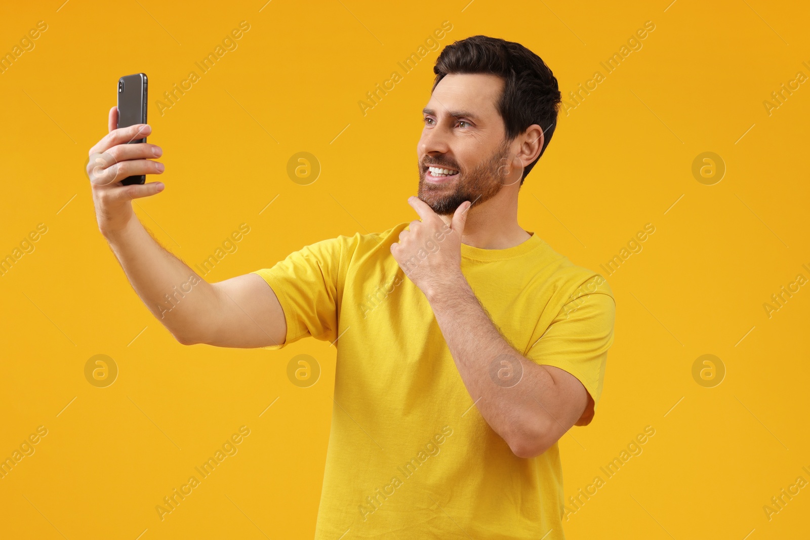 Photo of Smiling man taking selfie with smartphone on yellow background