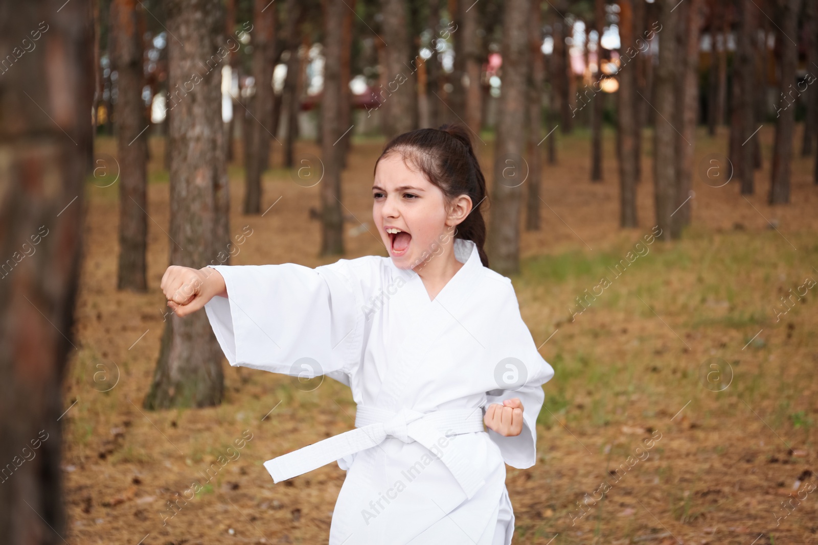 Photo of Cute little girl in kimono practicing karate in forest