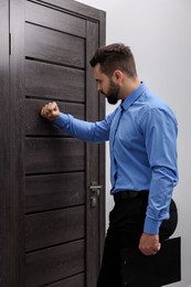 Photo of Collection agent in blue shirt knocking on wooden door