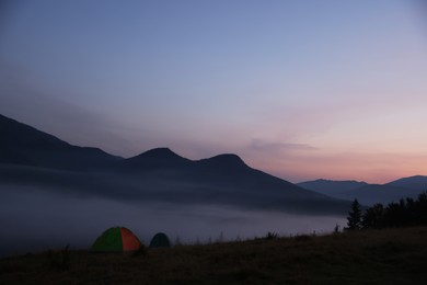 Photo of Picturesque view of mountain landscape with thick fog and camping tents at sunset