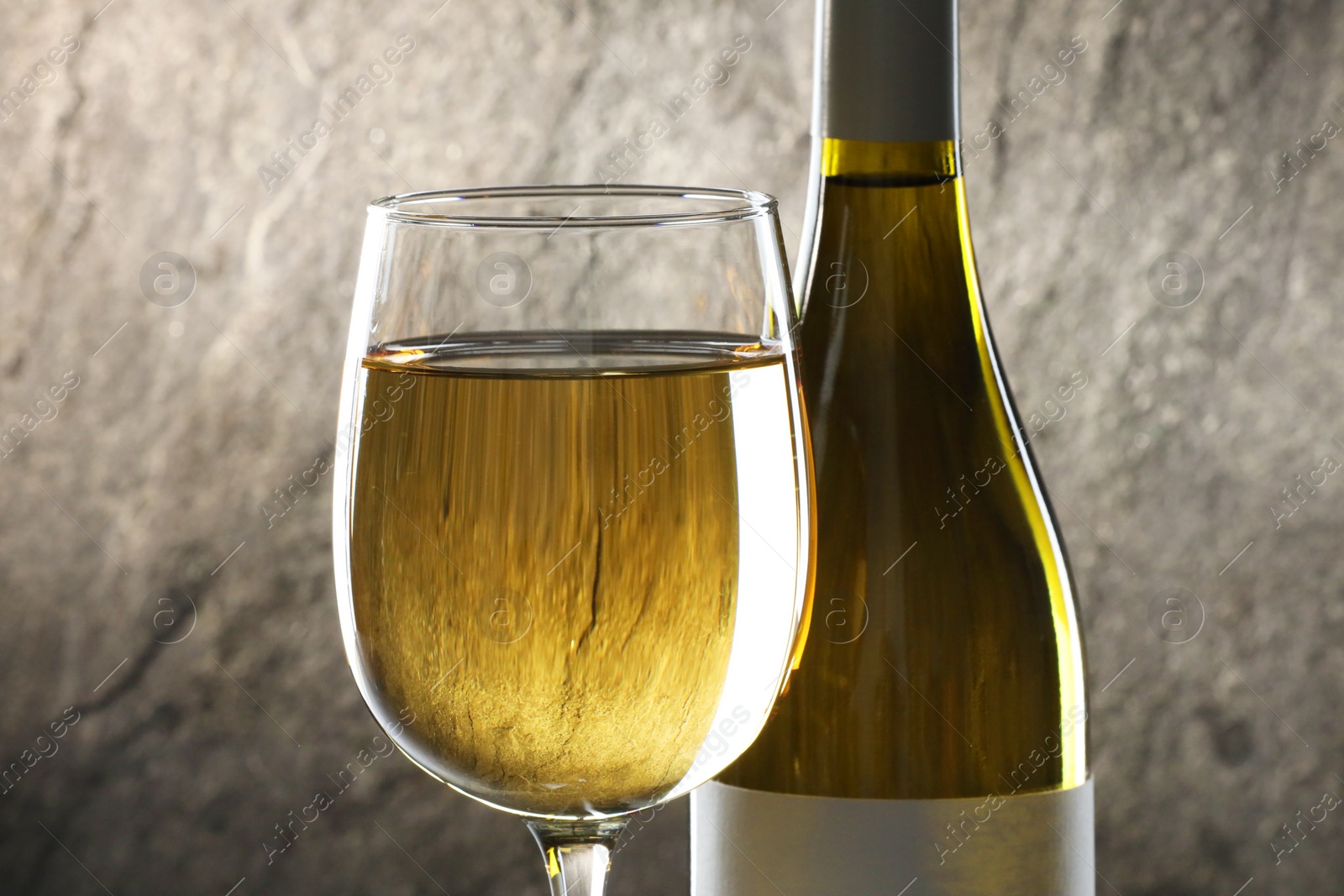 Photo of White wine in glass and bottle against grey background, closeup