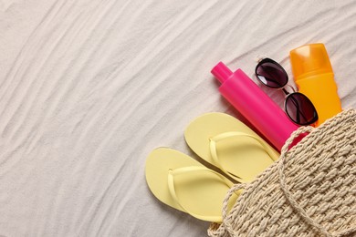 Photo of Wicker beach bag with sunscreen, flip flops and sunglasses on sand, flat lay. Space for text