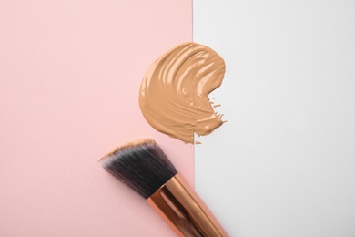 Sample of liquid foundation and makeup brush on color background, top view