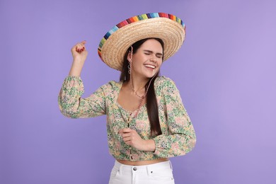 Photo of Young woman in Mexican sombrero hat dancing on violet background