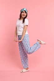 Happy woman in pyjama and sleep mask on pink background