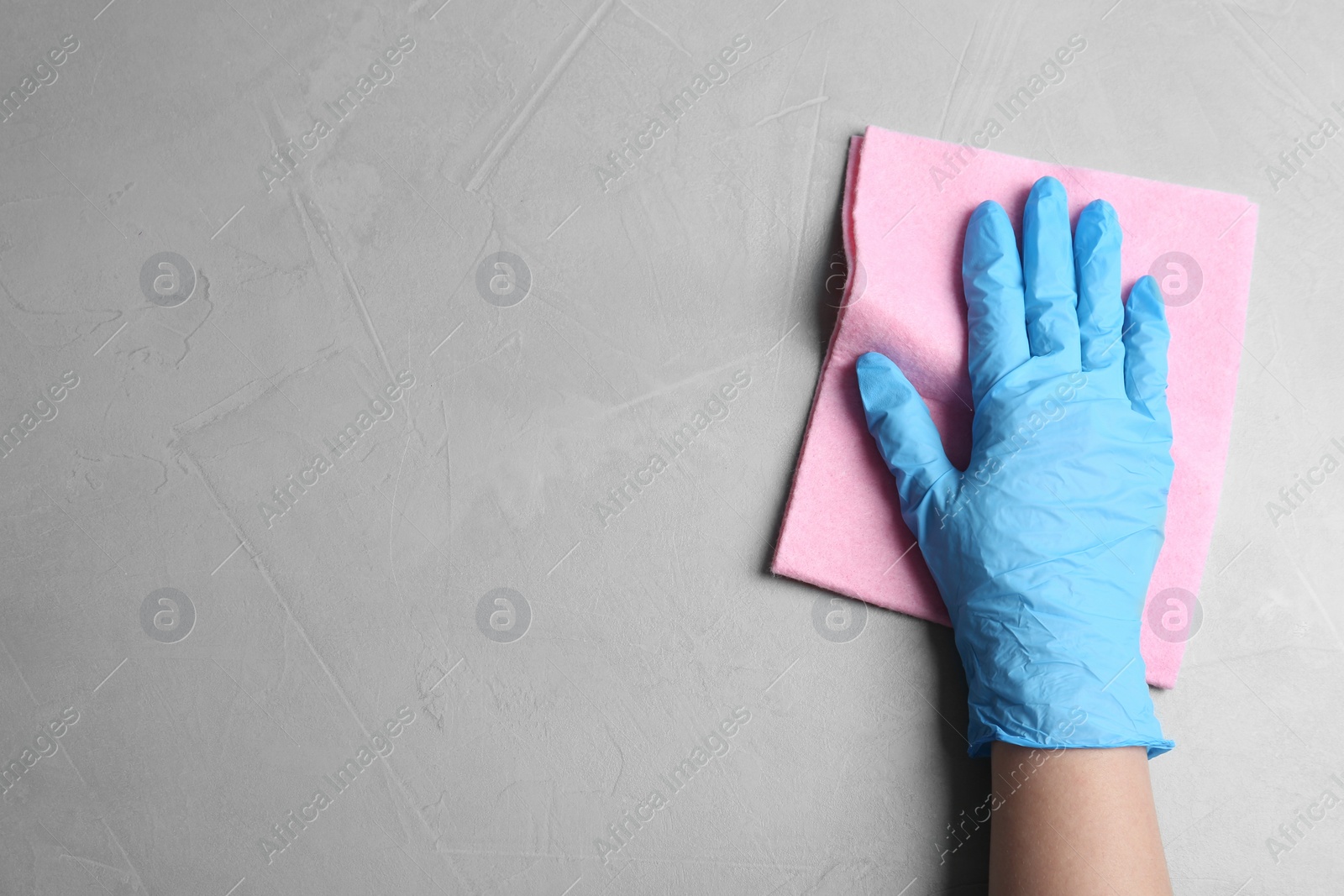 Photo of Woman in gloves wiping grey table with rag, top view. Space for text