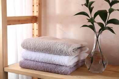 Photo of Stacked soft towels and green leaves on wooden shelf indoors