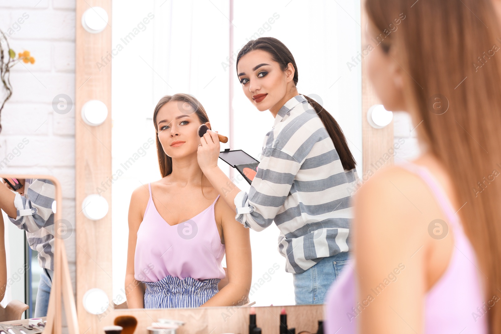 Photo of Professional visage artist applying makeup on woman's face in salon