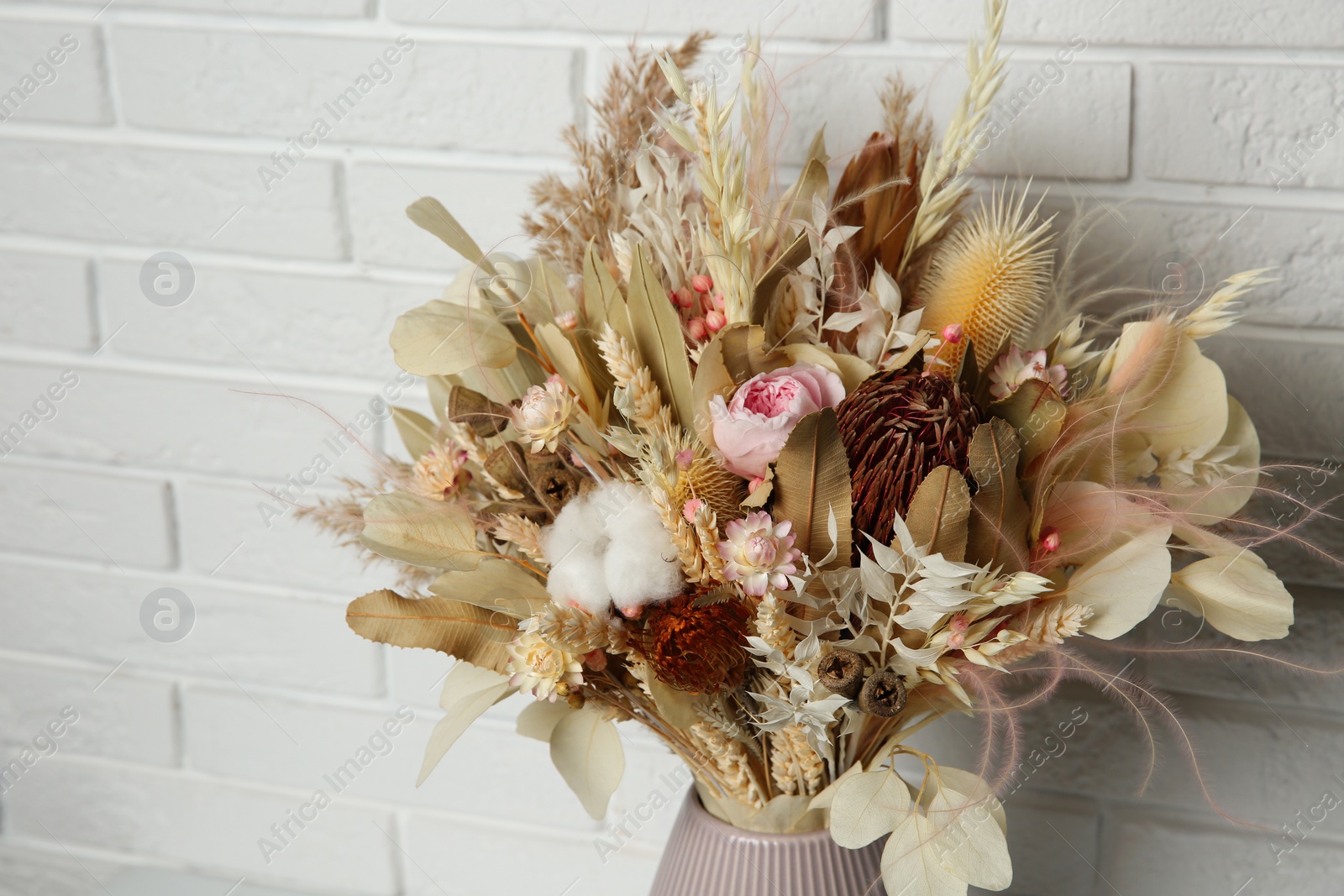 Photo of Beautiful dried flower bouquet in ceramic vase near white brick wall, closeup