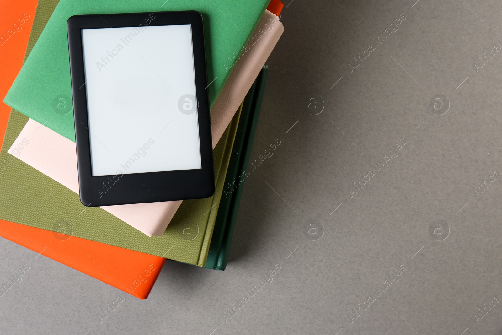 Photo of Modern e-book reader and stack of hard cover books on light grey table, top view. Space for text