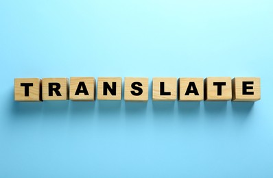 Photo of Wooden cubes with word Translate on light blue background, top view
