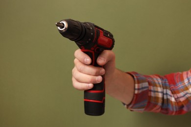 Photo of Handyman holding electric screwdriver on olive background, closeup