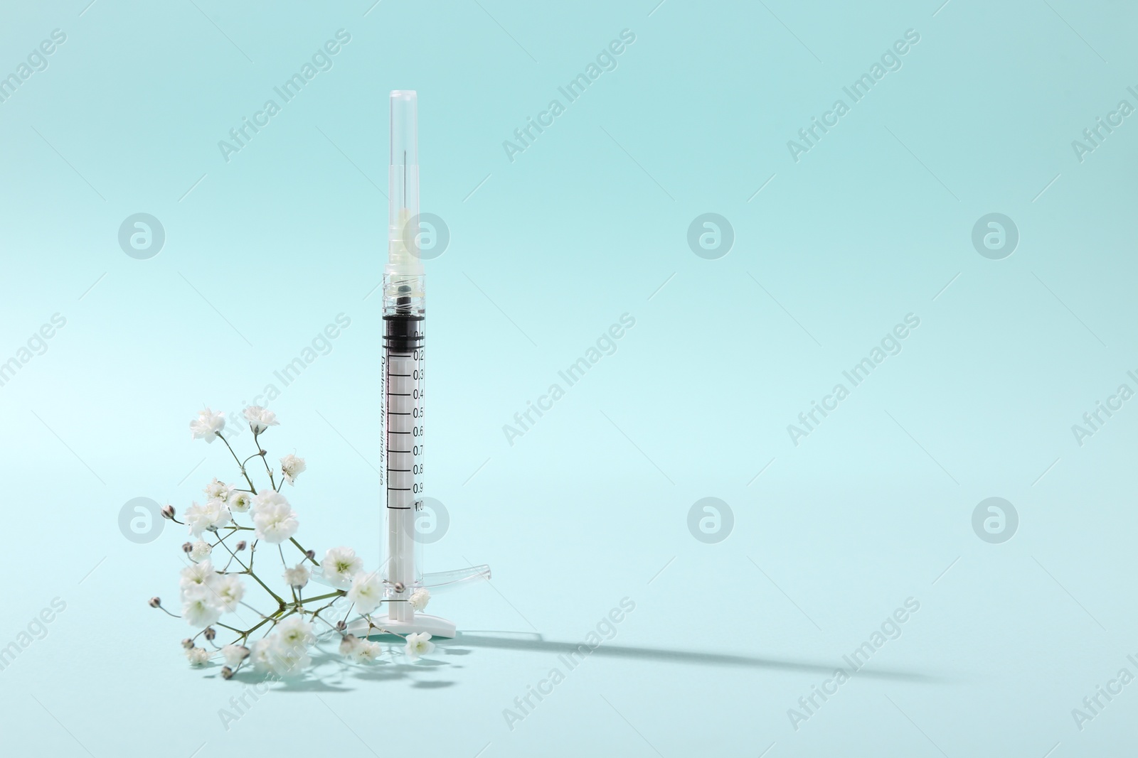 Photo of Cosmetology. Medical syringe and gypsophila on light blue background, space for text