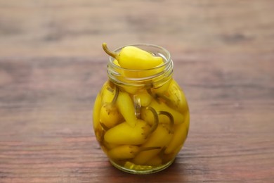 Glass jar of pickled yellow jalapeno peppers on wooden table