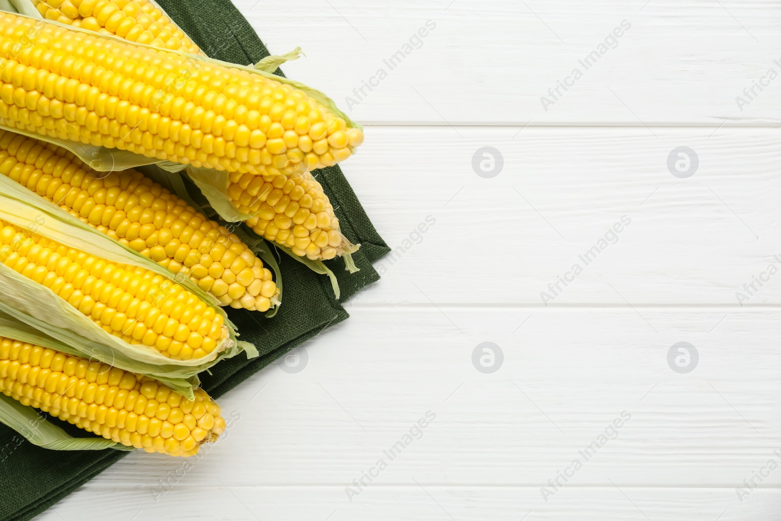 Photo of Tasty fresh corn cobs on white wooden table, top view. Space for text