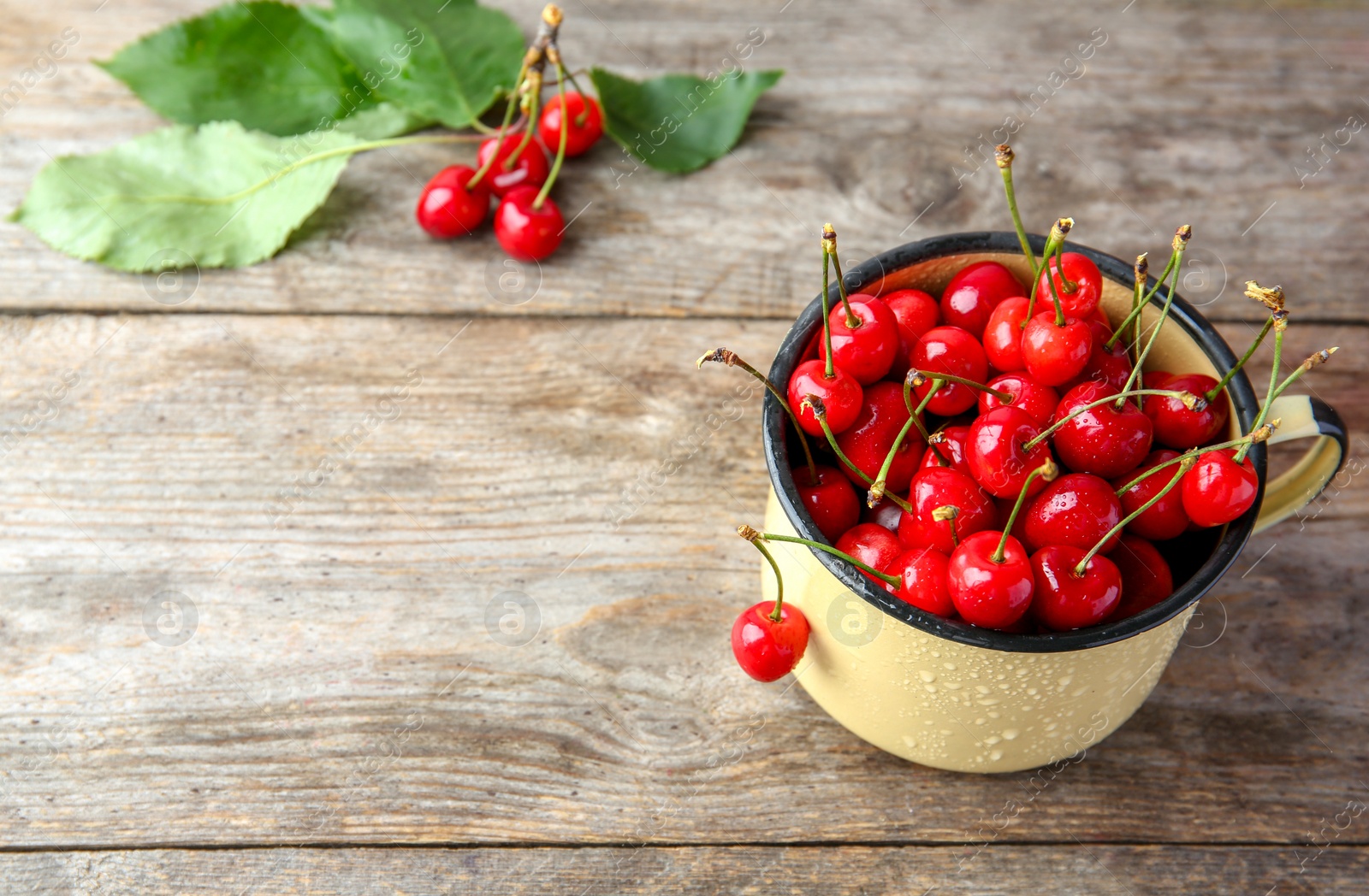 Photo of Metal mug with ripe red cherries on wooden table