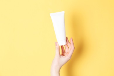 Photo of Woman holding tube of cream on yellow background, closeup