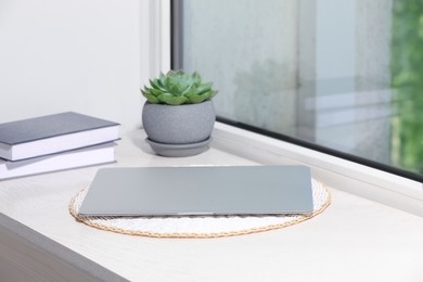 Photo of Laptop, books and succulent on wooden window sill