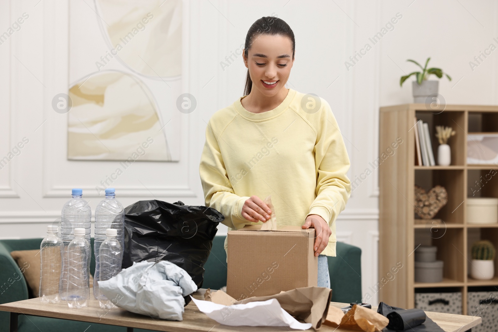 Photo of Smiling woman with cardboard box separating garbage in room