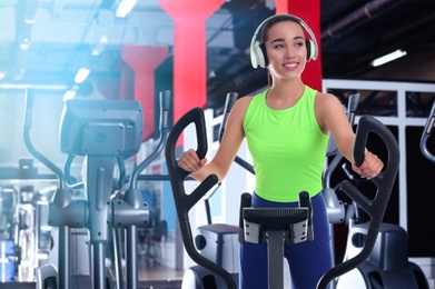 Image of Woman with headphones using modern elliptical machine in gym