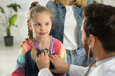 Photo of Mother and daughter having appointment with doctor. Pediatrician examining patient with stethoscope in clinic