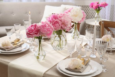 Stylish table setting with beautiful peonies and burning candles indoors