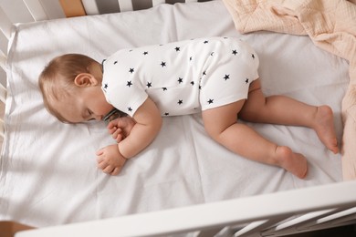 Photo of Adorable little baby with pacifier sleeping in crib, above view