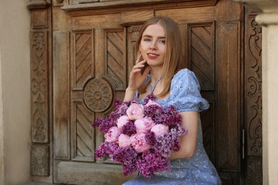 Beautiful woman with bouquet of spring flowers near building outdoors, space for text