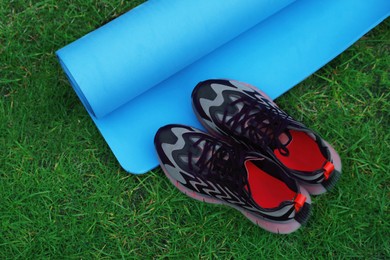 Photo of Blue karemat or fitness mat and sneakers on green grass outdoors, top view