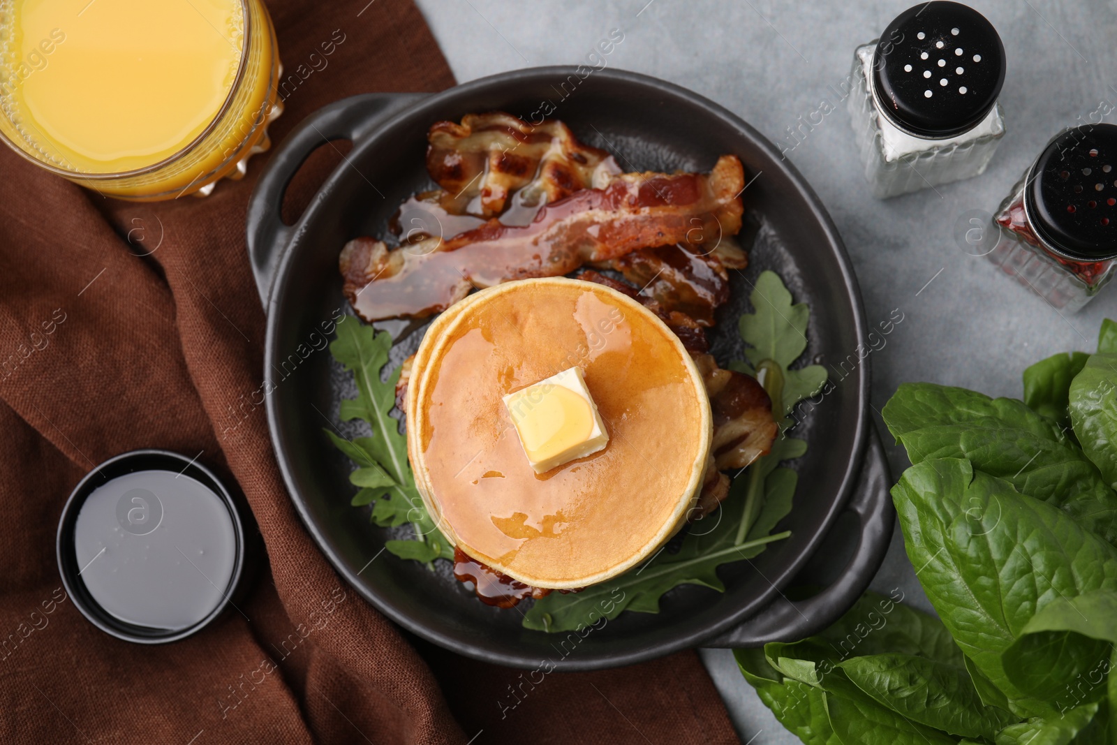 Photo of Tasty pancakes with butter, fried bacon and fresh arugula on grey table, flat lay