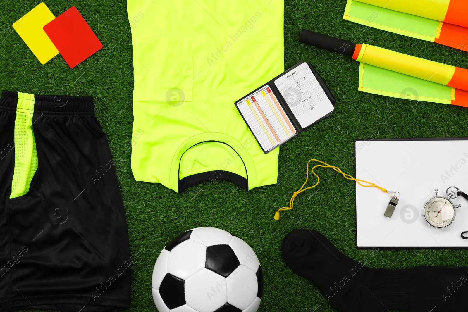 Photo of Uniform, soccer ball and other referee equipment on green grass, flat lay