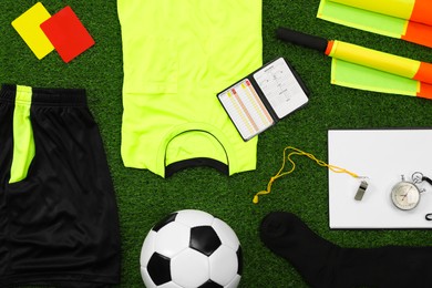 Uniform, soccer ball and other referee equipment on green grass, flat lay