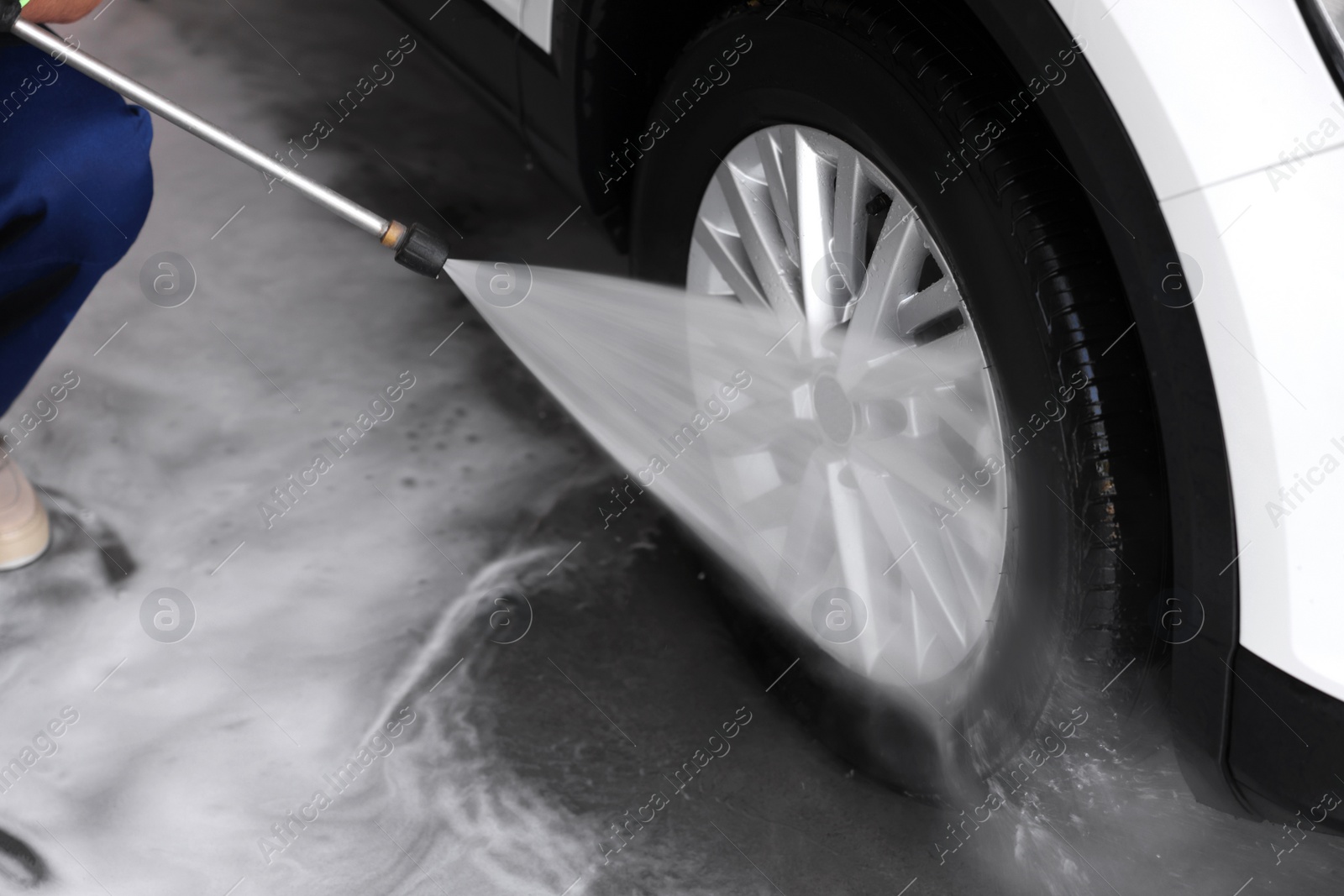 Photo of Worker washing auto with high pressure water jet at outdoor car wash, closeup