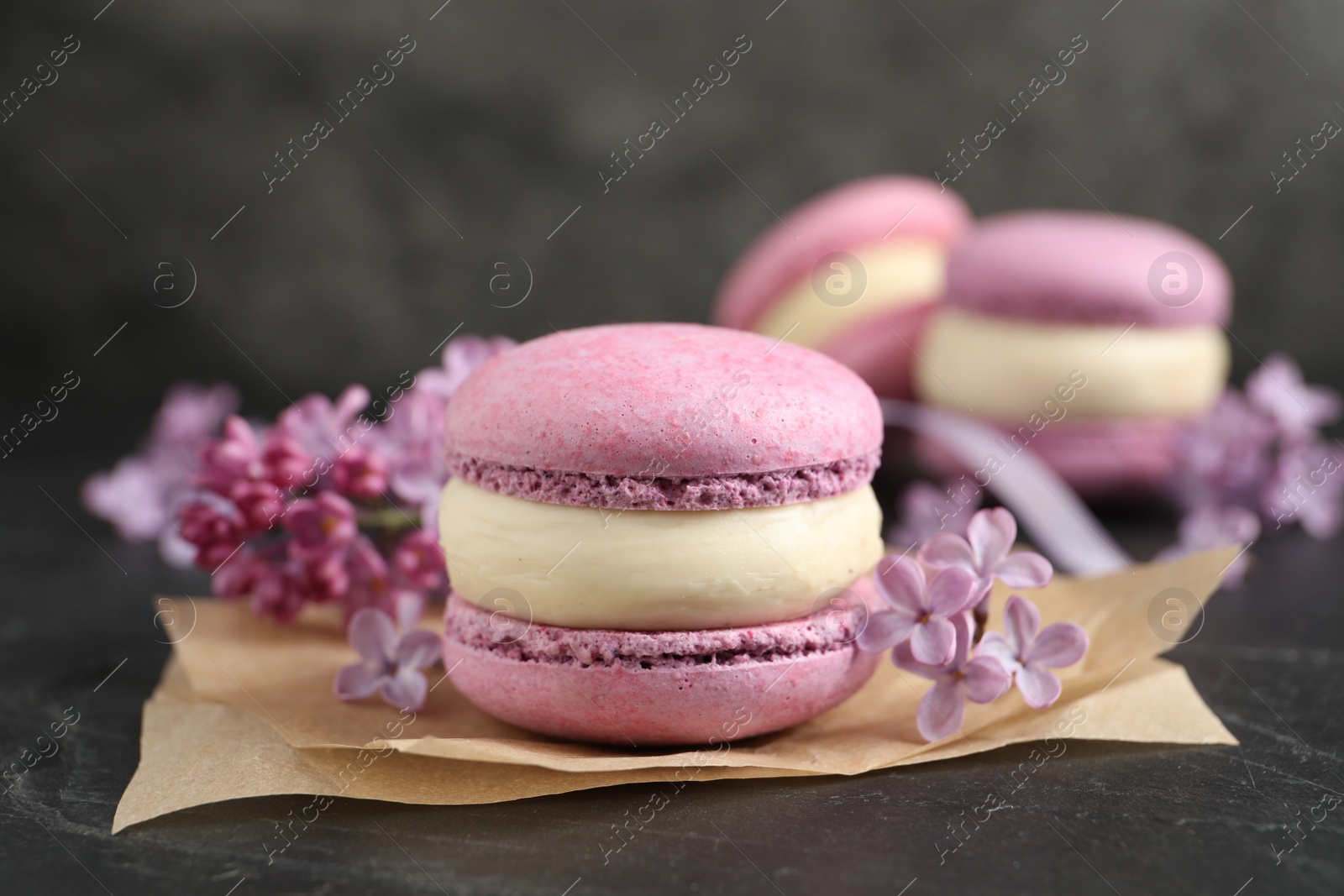 Photo of Delicious violet macaron and lilac flowers on black table, closeup