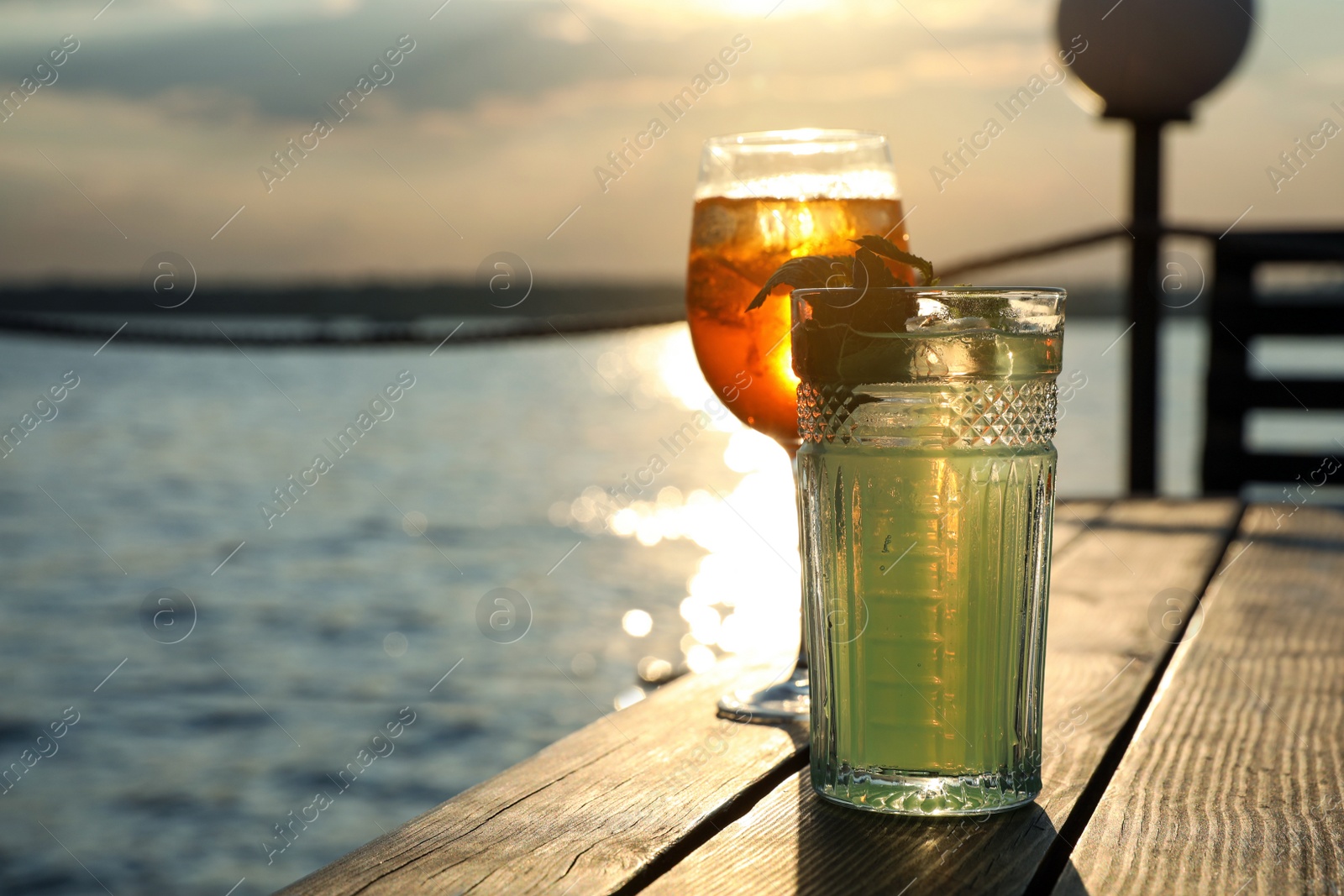 Photo of Glasses of fresh summer cocktails on wooden table outdoors at sunset. Space for text