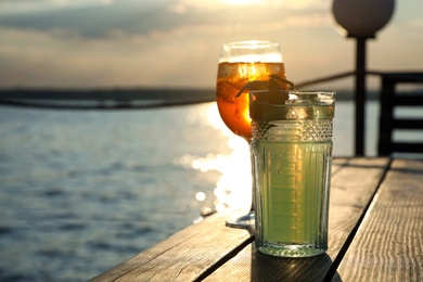 Glasses of fresh summer cocktails on wooden table outdoors at sunset. Space for text