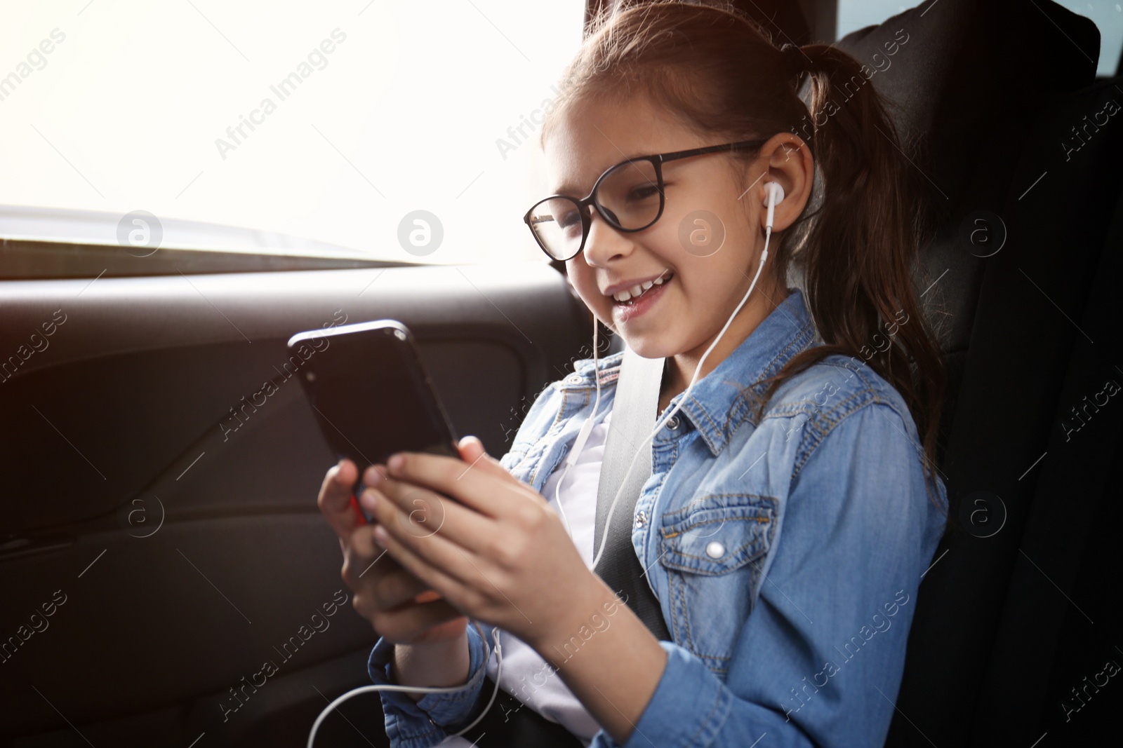 Photo of Cute little girl listening to audiobook in car