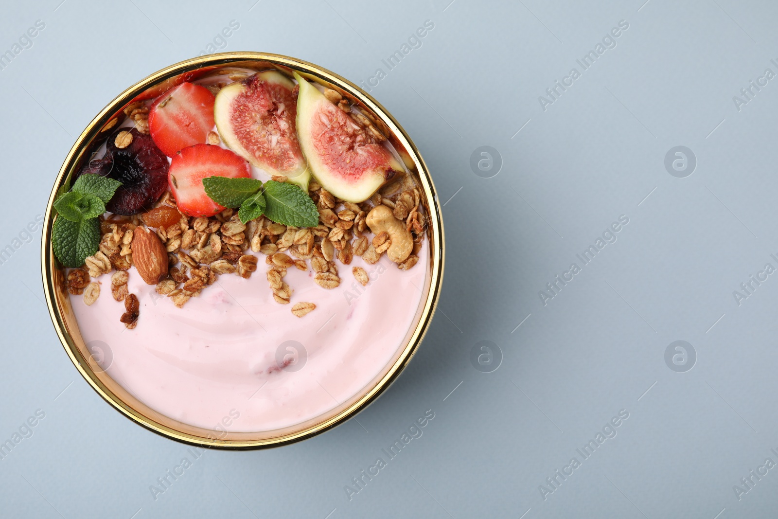 Photo of Bowl with yogurt, fruits and granola on light grey background, top view. Space for text