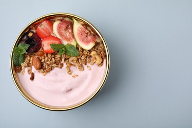 Photo of Bowl with yogurt, fruits and granola on light grey background, top view. Space for text