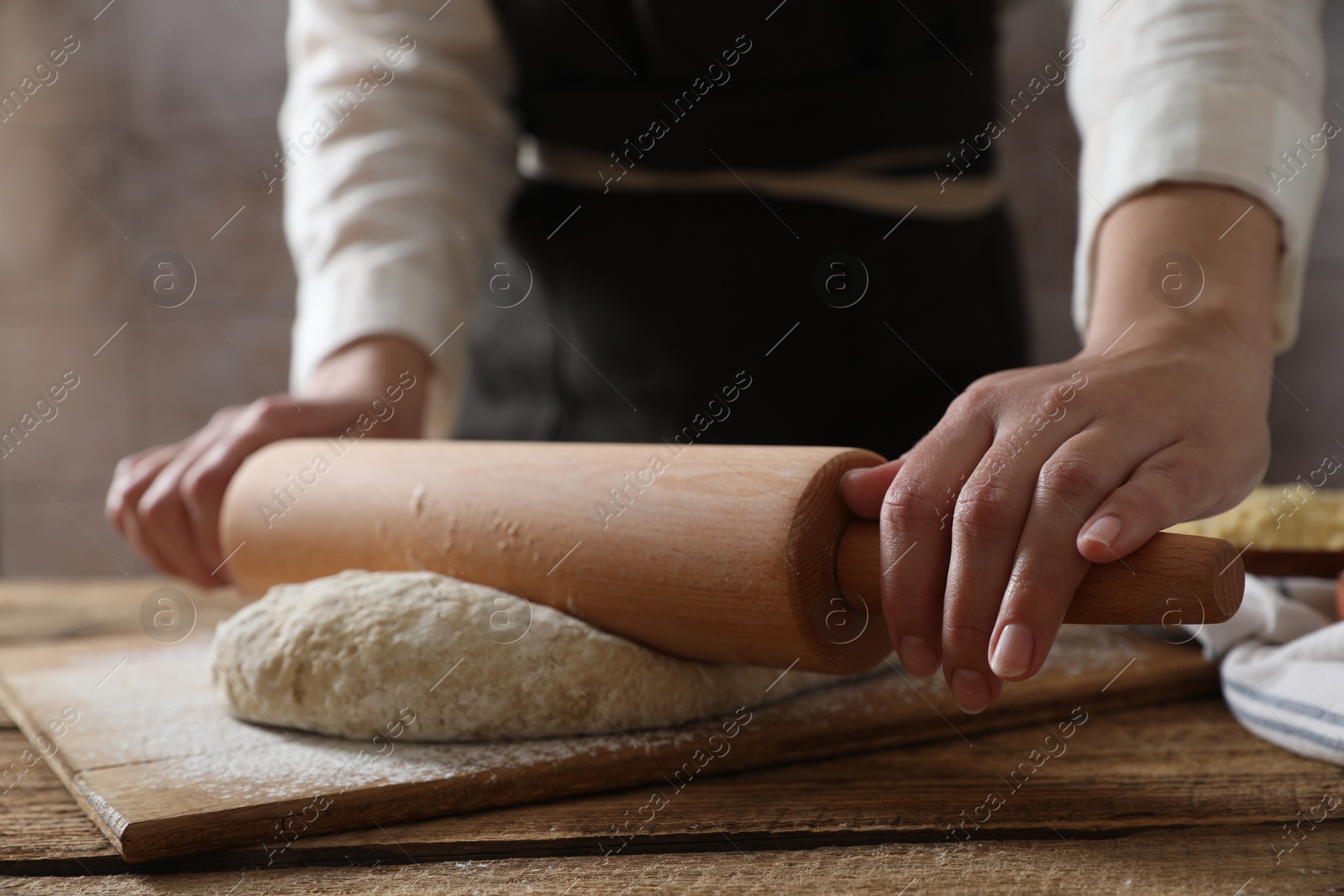 Photo of Woman rolling raw dough at wooden table, closeup